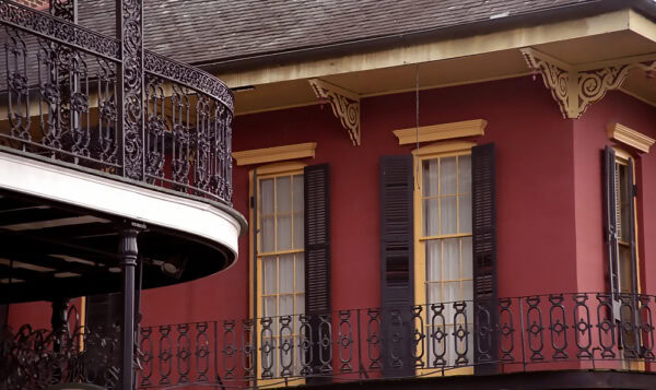French Quarter, New Orleans, ornate cast iron balconies overlap, red building with tall yellow windows with black shutters in the background