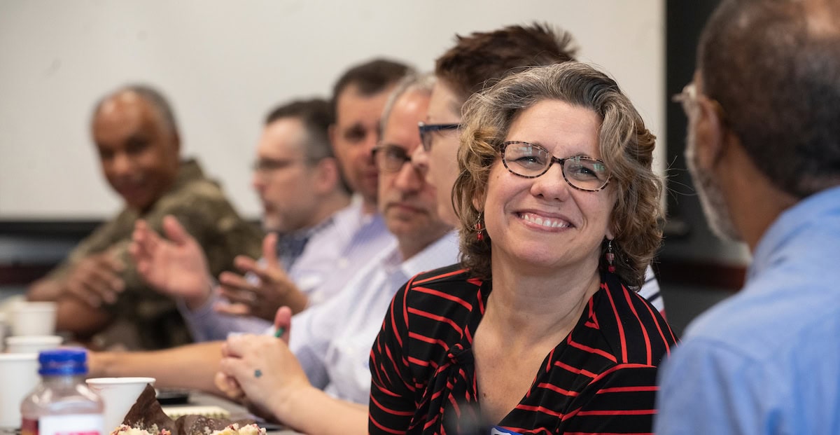 A woman in a striped shirt at a table smiling with several people sitting next to her.