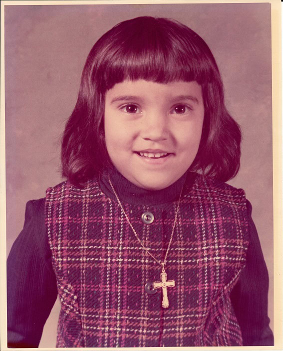 A child in a plaid vest with a cross necklace posing for a school photo