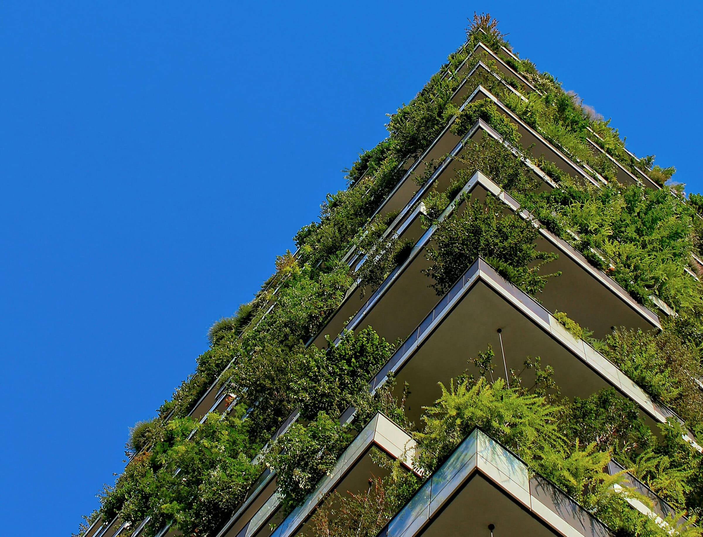 Green vegetation hangs off every level of a skyscraper, set against a clear blue sky.