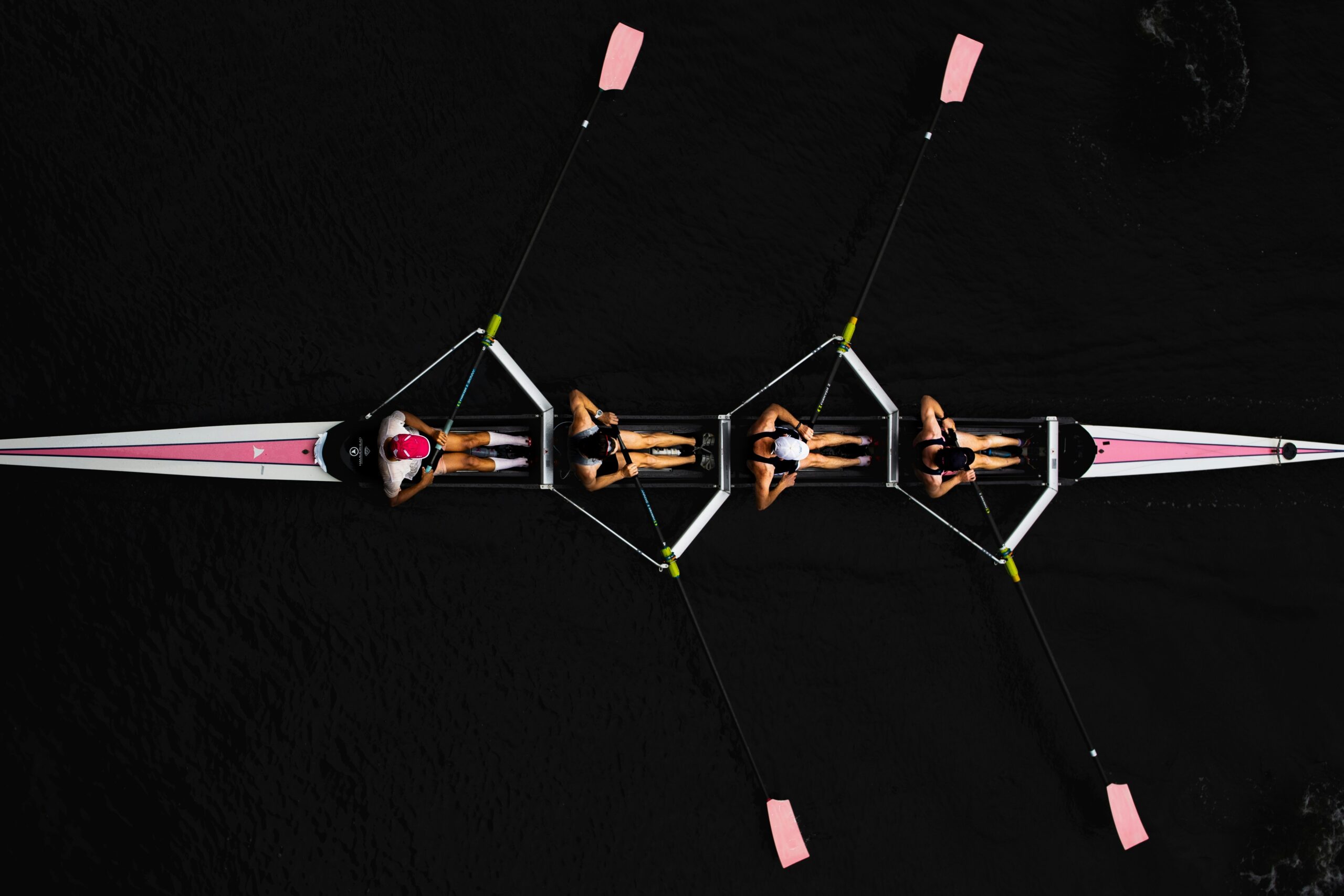 A bird's eye view of four people rowing in a pink skull boat
