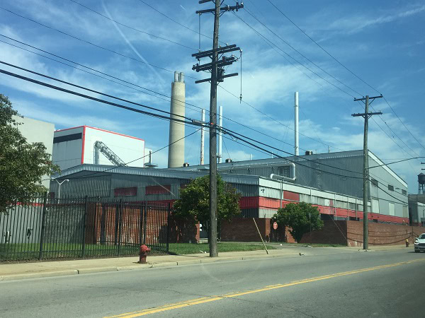 A factory with a prominent chimney stands alongside a road