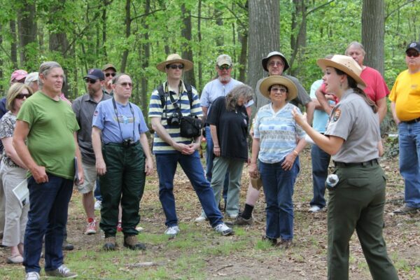 NPS guide leading a large tour group surrounded by trees