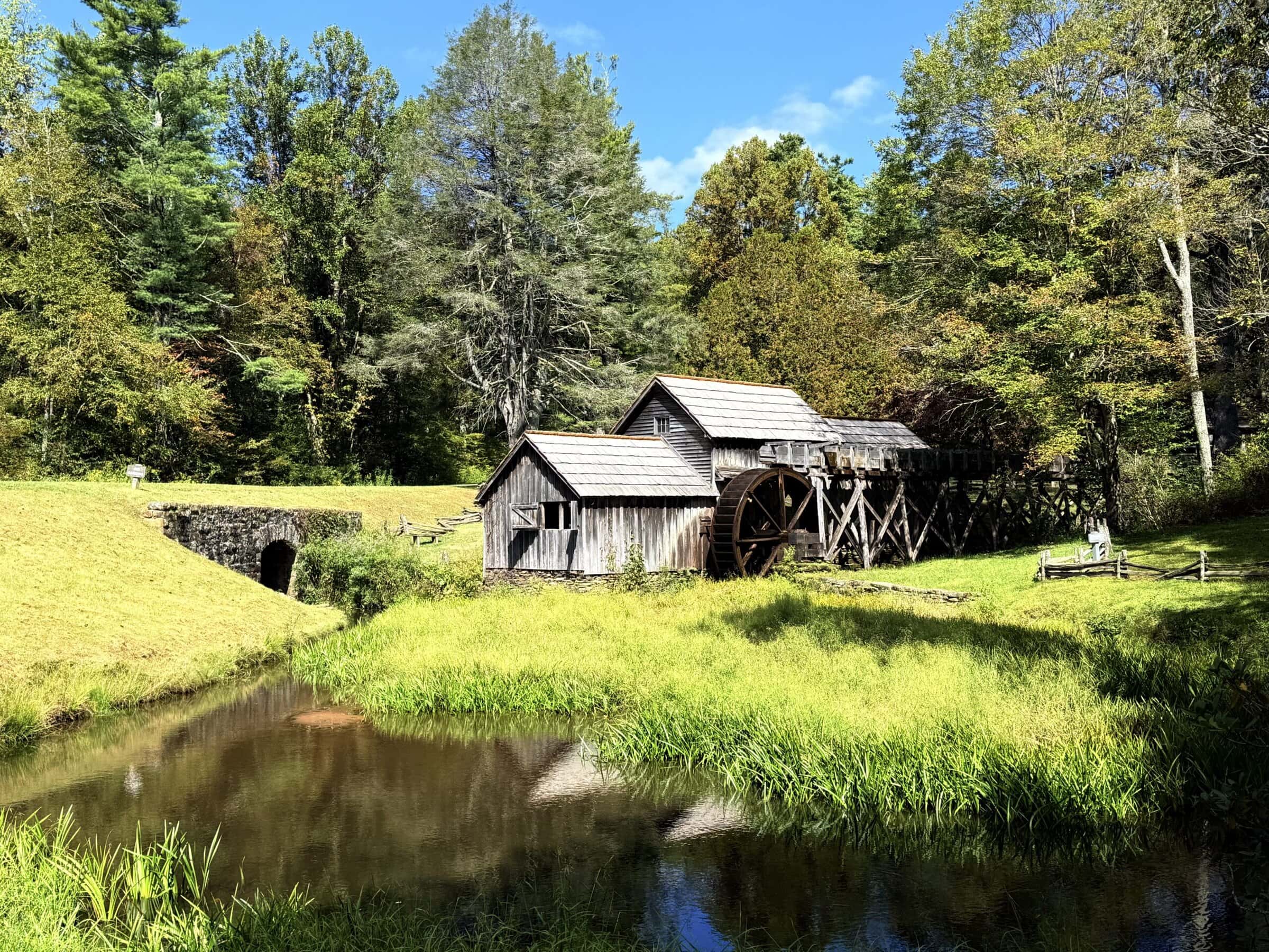 A small building and mill surrounded by grass and large trees