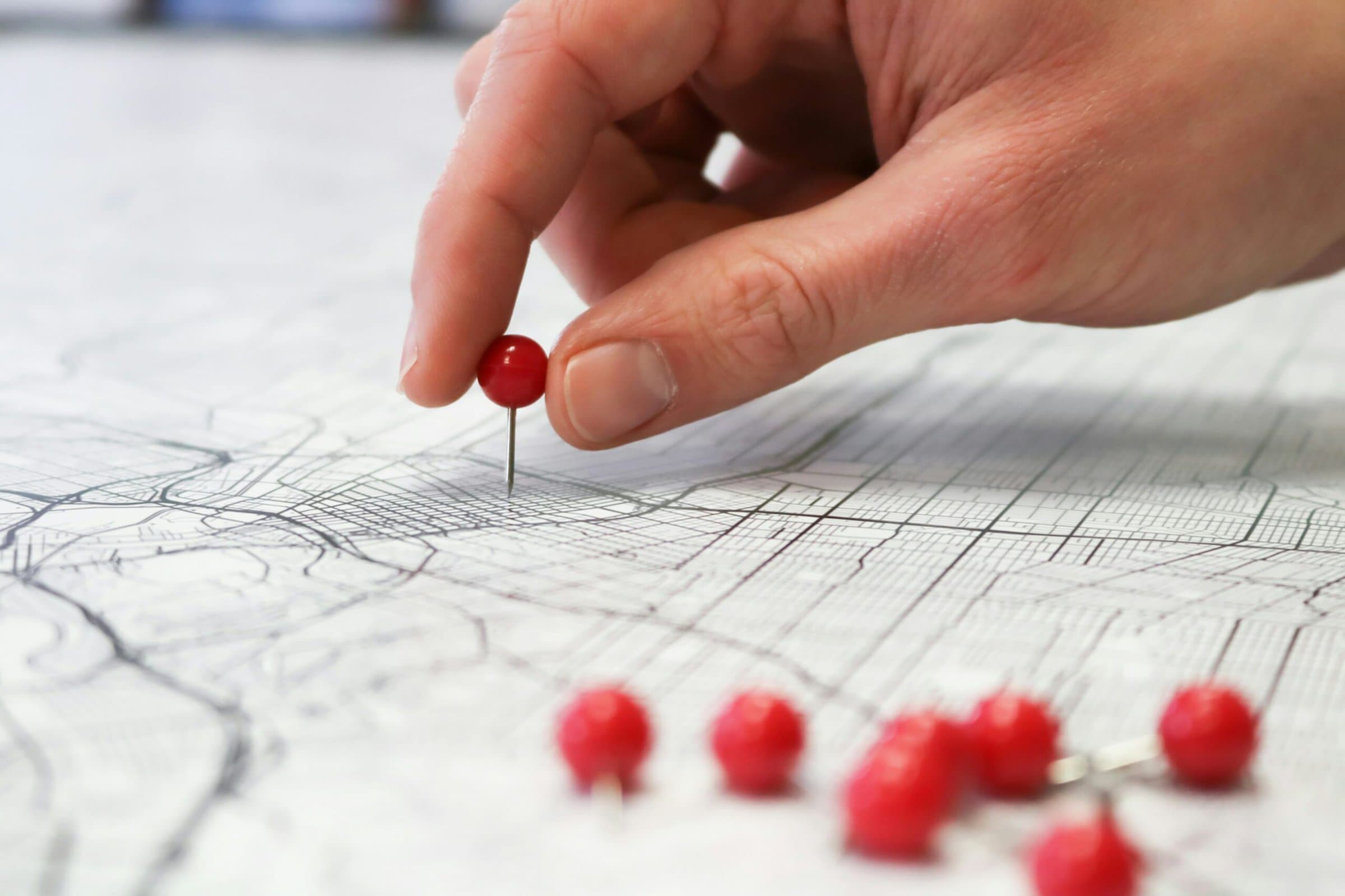 Hand placing a red pushpin on a black and white map