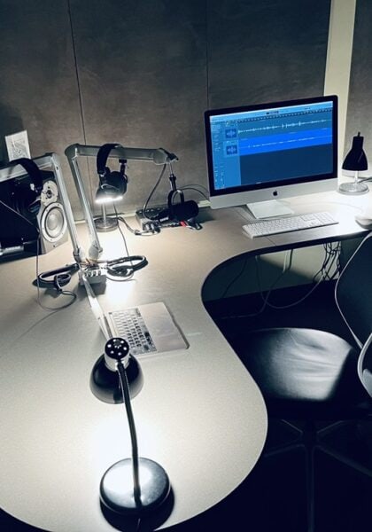 A L-shaped desk with speakers, microphones, headsets, computers, and chairs.